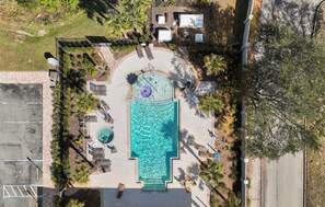 Eine Vogelperspektive zeigt einen Urlaubsort mit einem zentral gelegenen Swimmingpool, Liegestühlen und einer kleinen, runden Whirlwanne.