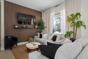 Ein modernes Wohnzimmer mit einer Couch, einem Couchtisch, einem schwarzen Sessel, einem großen Spiegel und einer Topfpflanze.