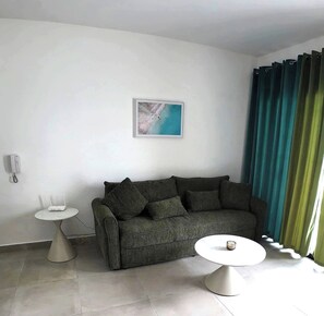 A modern living room with a grey sofa, a small white table, and a round coffee table. - Charming Bayahíbe Apartment Comfort Pool, Beach Access (San Rafael del Yuma)
