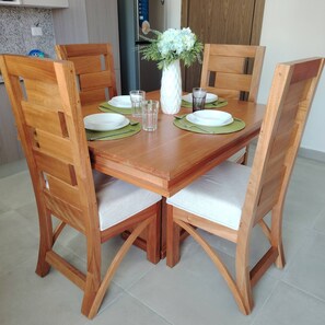 A wooden dining table with four chairs, a vase with flowers, and two glasses. - Charming Bayahíbe Apartment Comfort Pool, Beach Access (San Rafael del Yuma)