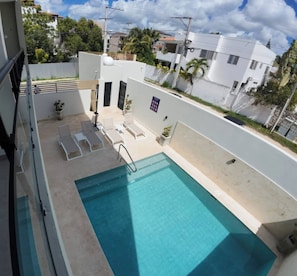 A rooftop swimming pool with lounge chairs, a small garden area, and a view of surrounding buildings. - Charming Bayahíbe Apartment Comfort Pool, Beach Access (San Rafael del Yuma)