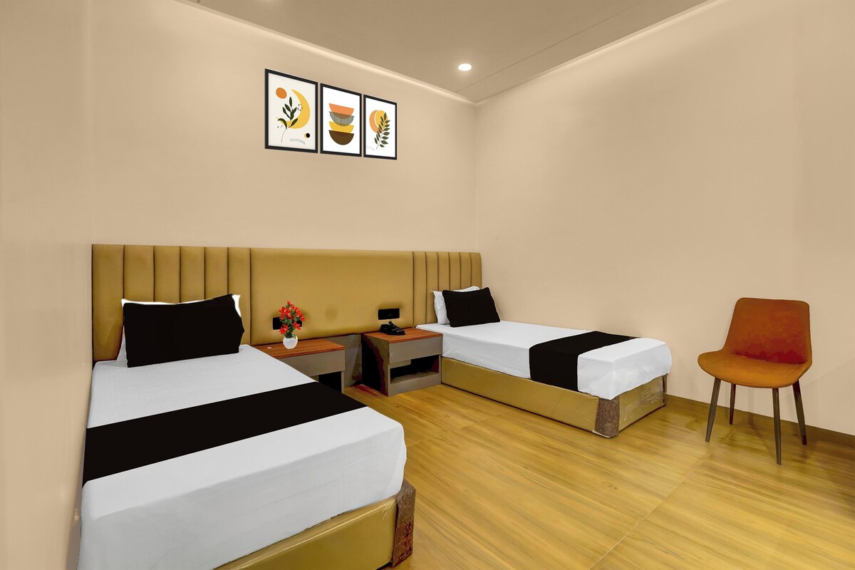 A hotel room with two beds, a nightstand, a chair, and wall art.