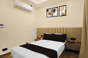 Habitación de hotel con cama, mesita de noche, aire acondicionado instalado en la pared y tres obras de arte enmarcadas.