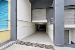 A narrow, enclosed corridor with a metal grate at the bottom, flanked by walls with different textures and colors, leading to a door at the end.