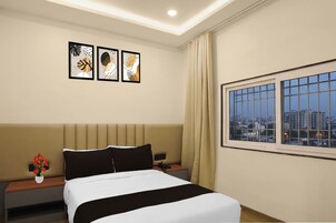 Habitación de hotel con cama, mesita de noche, un jarrón con flores y tres cuadros en la pared.