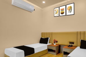A hotel room with two beds, a bedside table with a phone, a small plant, and a wall-mounted air conditioner.