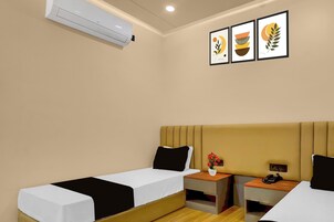 A hotel room with two beds, a bedside table with a phone, a small plant, and a wall-mounted air conditioner.