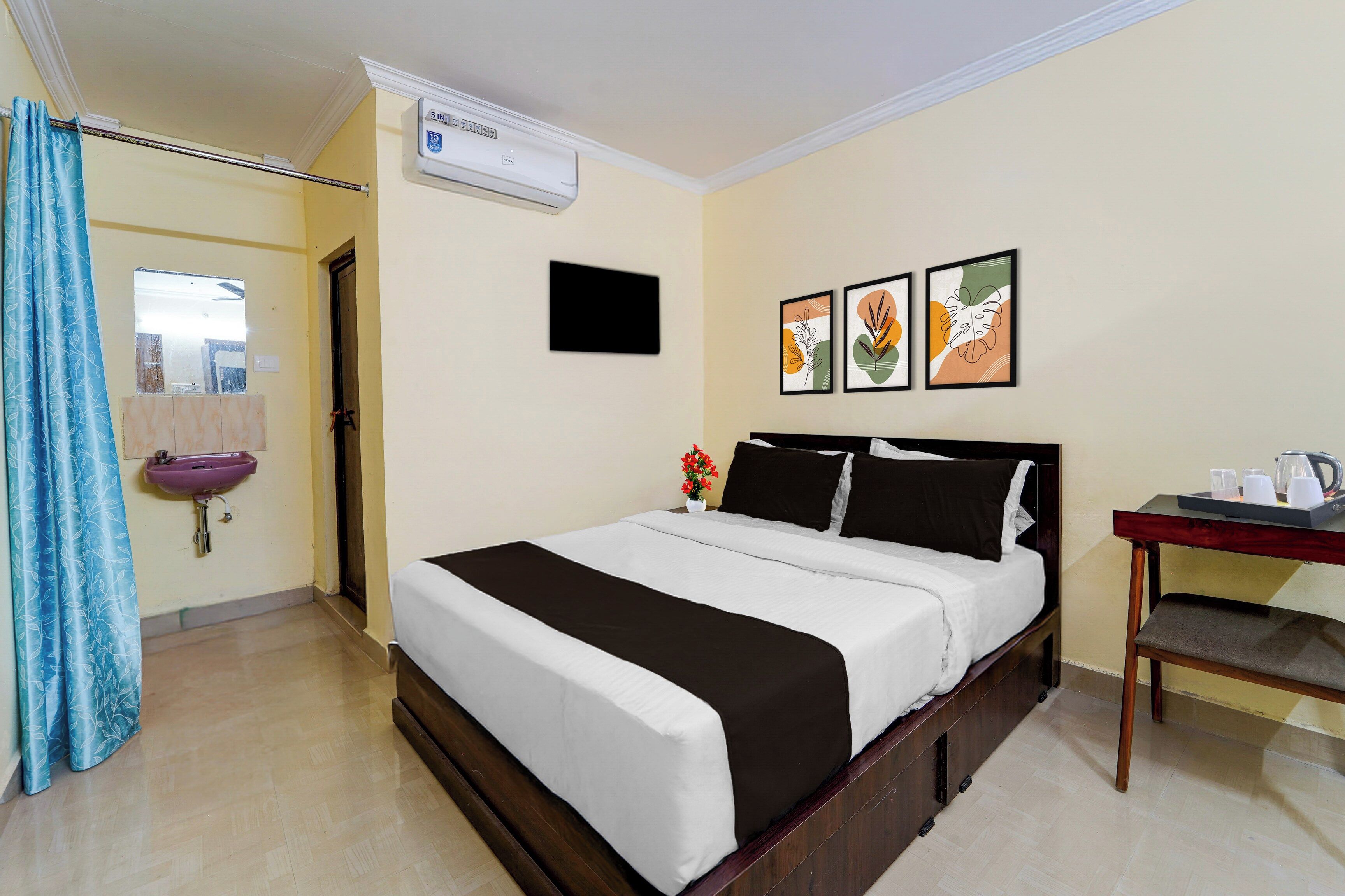 A hotel room with a bed, a bedside table with a kettle, a sink, and a shower curtain.