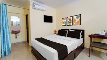 A hotel room with a bed, a bedside table with a kettle, a sink, and a shower curtain.