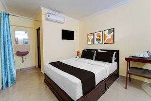 A hotel room with a bed, a bedside table with a kettle, a sink, and a shower curtain.