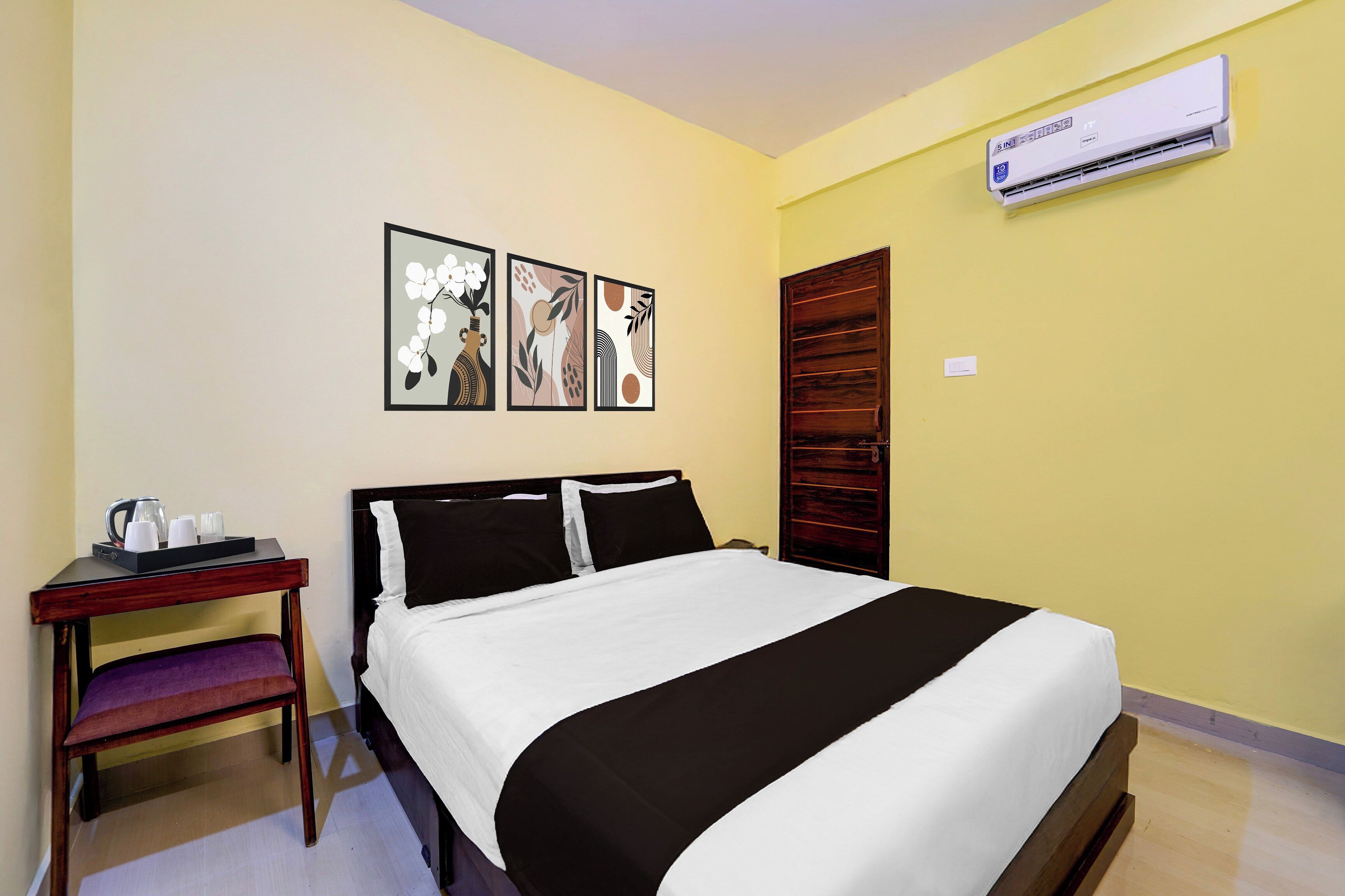 A hotel room with a bed, a desk with a coffee maker, and an air conditioning unit on the wall.