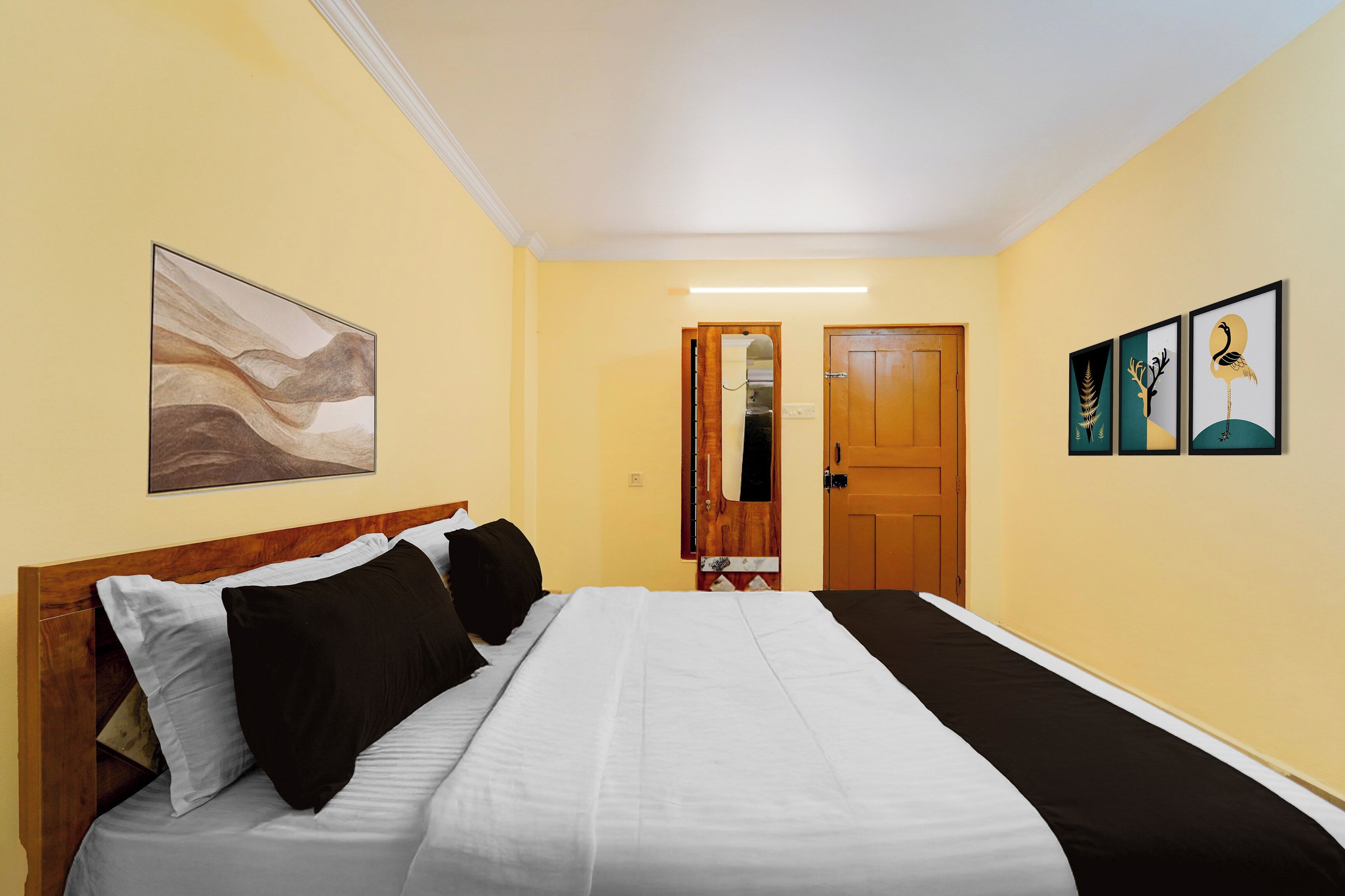 A hotel room with a bed, a wooden headboard, a door, and two framed artworks on the wall.