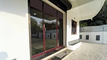 A modern building with a glass door entrance, a gravel driveway, and a small red mat at the door.