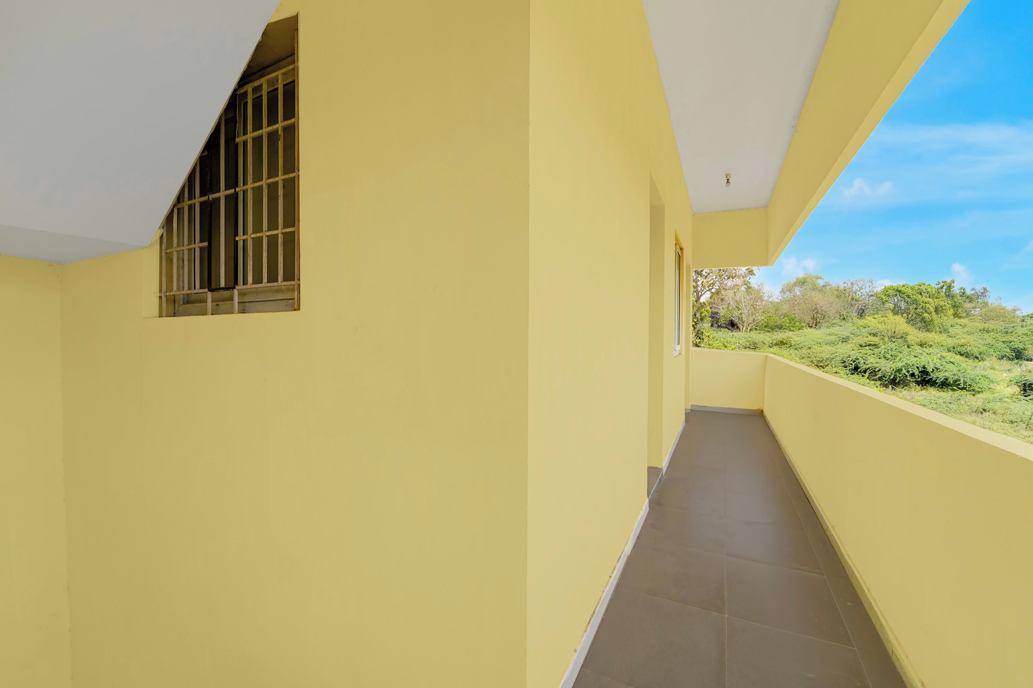 Un pasillo con paredes amarillas, una ventana con barrotes y vistas al exterior con vegetación.