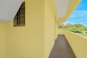 A corridor with yellow walls, a window with metal bars, and a view of greenery outside. - Hotel O Narsampathi Lakeview Coimbatore (Coimbatore)
