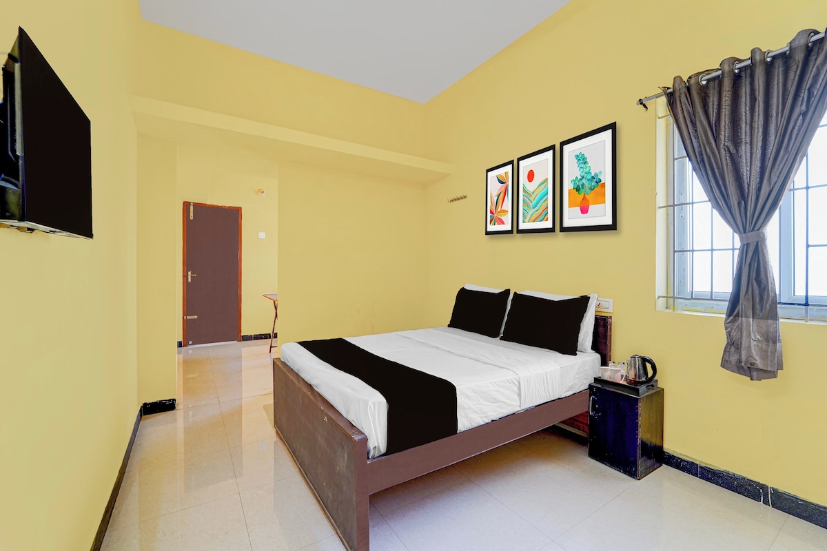 A hotel room with a bed, a window with curtains, a flat-screen TV mounted on the wall, and artwork on the wall.