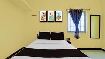 A hotel room with a bed, a window with curtains, and three framed artworks on the wall.