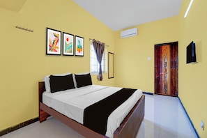 A bedroom with a bed, a window with curtains, a wall-mounted air conditioner, and a door with a decorative panel.