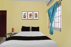 A bedroom with a bed, a nightstand, a vase with flowers, and three framed pictures on the wall.