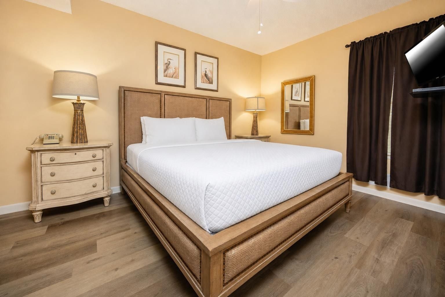 A hotel room with a large bed, bedside tables, a lamp, a mirror, and artwork on the wall.