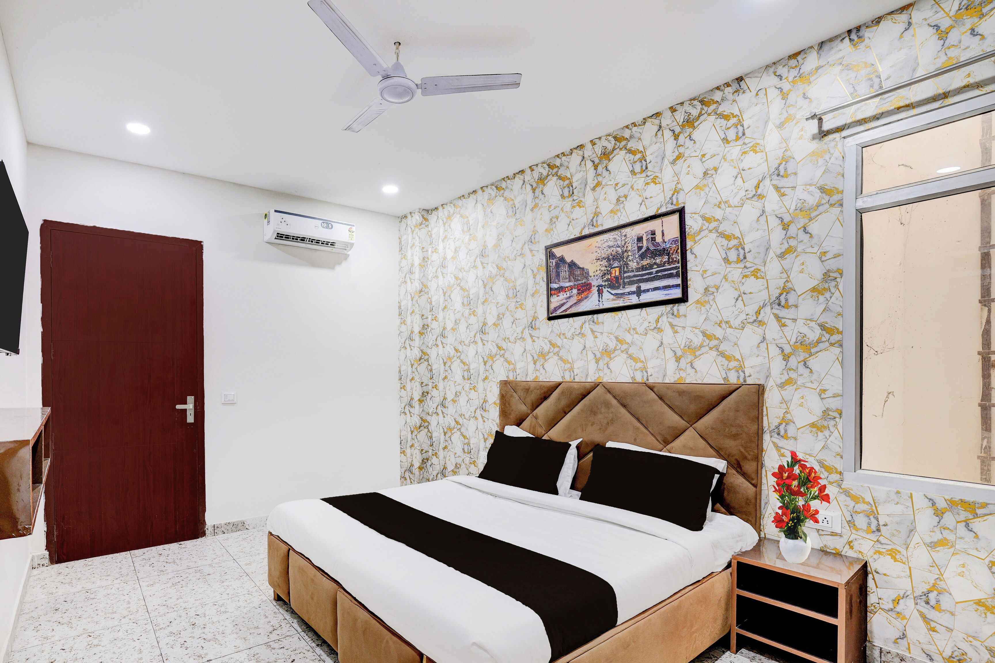 A bedroom with a bed, a ceiling fan, an air conditioning unit, a window, and a wall with a patterned wallpaper.