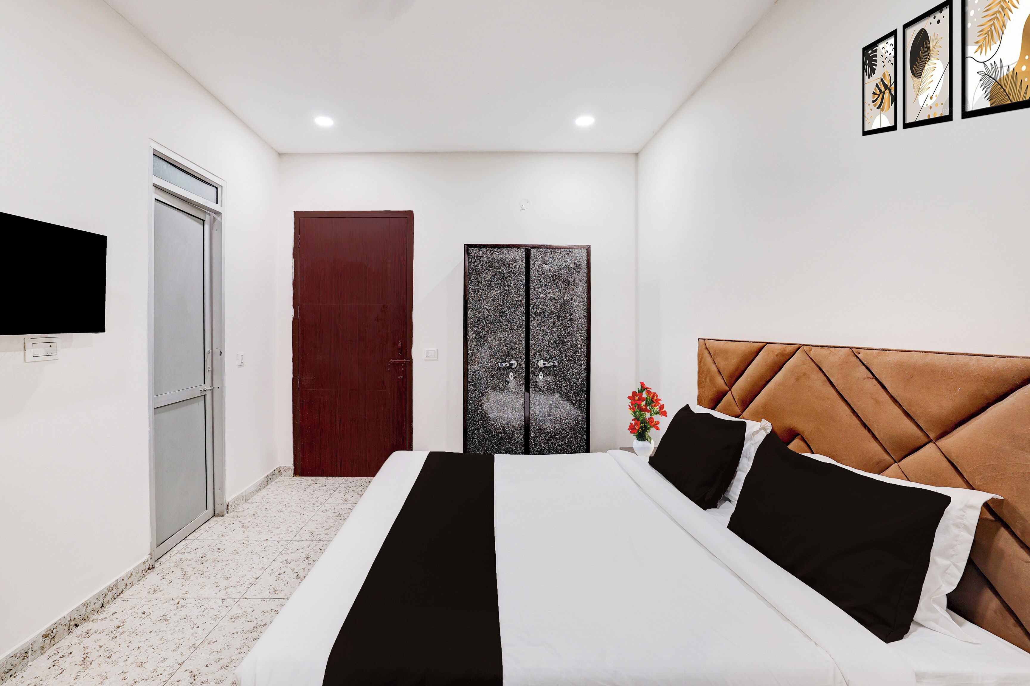 A bedroom with a bed, a TV mounted on the wall, a door, and a wall-mounted artwork.