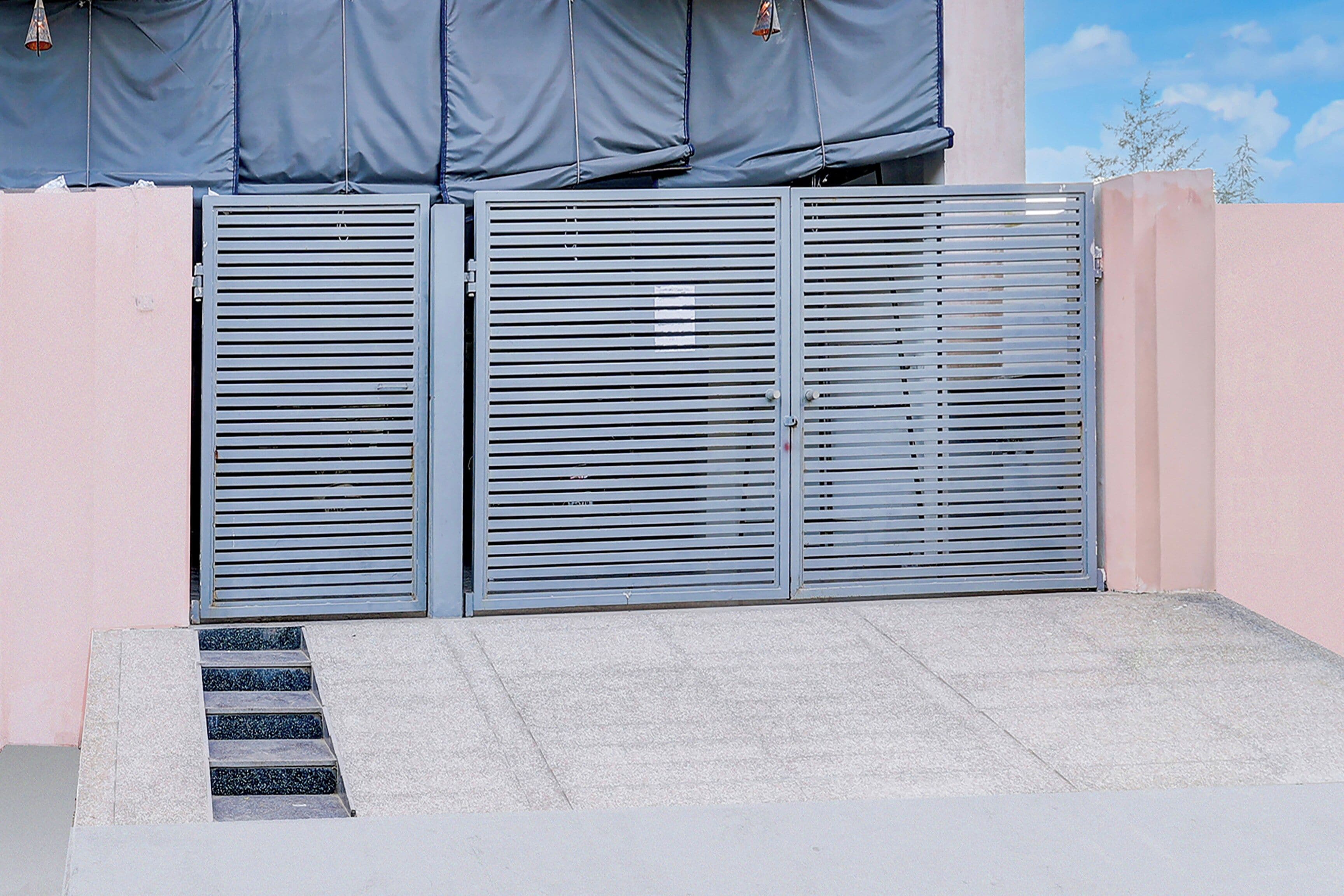 A metal gate with horizontal slats, a concrete step leading up to it, and a pink wall in the background.