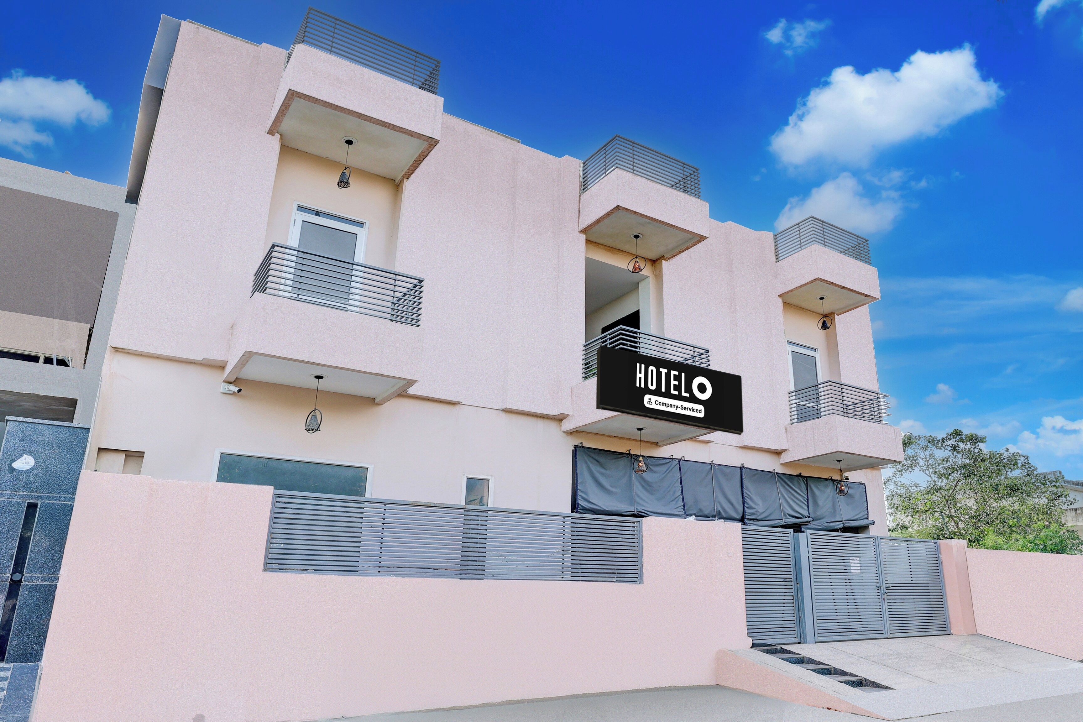 Edifício de hotel com placa indicando serviço corporativo, várias varandas e entrada com portão.