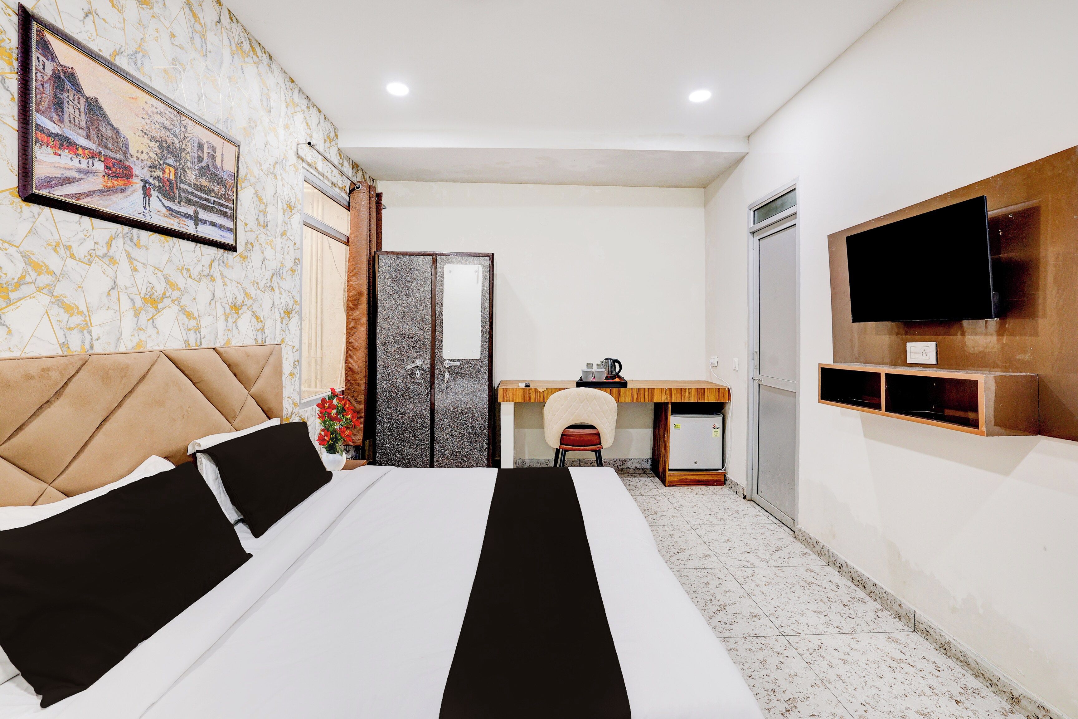 Quarto de hotel com cama, escrivaninha, televisão e espelho.