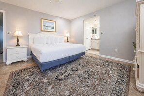 Ein Schlafzimmer mit Bett, Nachttischen, einem Teppich, einem gerahmten Bild an der Wand und einem durchgehenden Tür geöffneten Badezimmer.