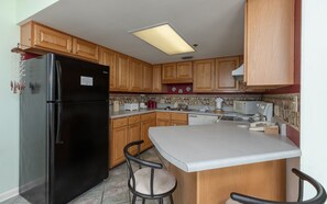 A kitchen with wooden cabinets, a black refrigerator, a microwave, and a small island with chairs. - Phoenix East 602 1 Bedroom Condo (Orange Beach)