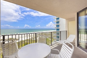 A balcony with a table and chairs, overlooking a beach with a clear sky. - Phoenix East 502 1 Bedroom Condo (Orange Beach)