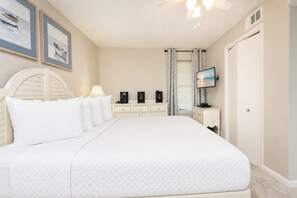Ein Schlafzimmer mit einem großen Bett, einem Nachttisch mit Lautsprechern, einem Fernseher und einem Fenster mit Vorhängen.