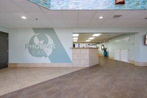 A spacious lobby with a reception desk, a wall-mounted logo, and a tiled floor. - Phoenix East 505 1 Bedroom Condo (Orange Beach)
