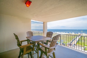 A balcony with a table and chairs, overlooking a beach with umbrellas and a view of the ocean. - Phoenix East 205 1 Bedroom Condo (Orange Beach)