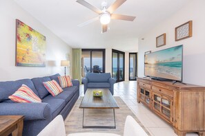 Ein Wohnzimmer mit einer Couch, Sesseln, einem Couchtisch, einem Fernseher und einem Deckenventilator.
