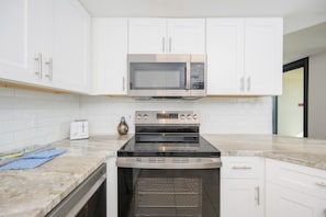 A kitchen with white cabinets, a microwave, a stove, and a toaster. - Phoenix East 205 1 Bedroom Condo (Orange Beach)