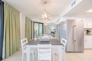A modern kitchen with a built-in refrigerator, a dining table with chairs, and a hanging light fixture. - Phoenix East 205 1 Bedroom Condo (Orange Beach)