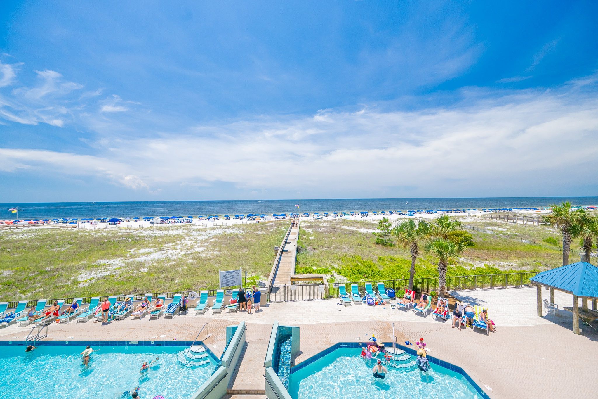 A beach resort with multiple swimming pools, sun loungers, and a boardwalk leading to the beach.