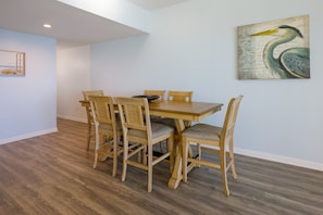 A dining area with a wooden table and chairs, a painting on the wall, and a window with a view. - Phoenix Ii 2141 3 Bedroom Condo (Orange Beach)