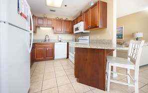 A kitchen with wooden cabinets, a white refrigerator, a microwave, and a dishwasher. - Phoenix East 1408 1 Bedroom Condo (Orange Beach)