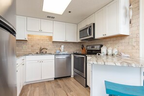 A kitchen with white cabinets, a microwave, a dishwasher, and a stove. - Phoenix East 705 1 Bedroom Condo (Orange Beach)