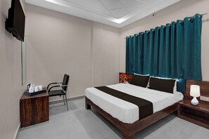 Ein Hotelzimmer mit einem Bett, einem Sessel, einem Nachttisch, einer Lampe und einem an der Wand befestigten Fernseher.