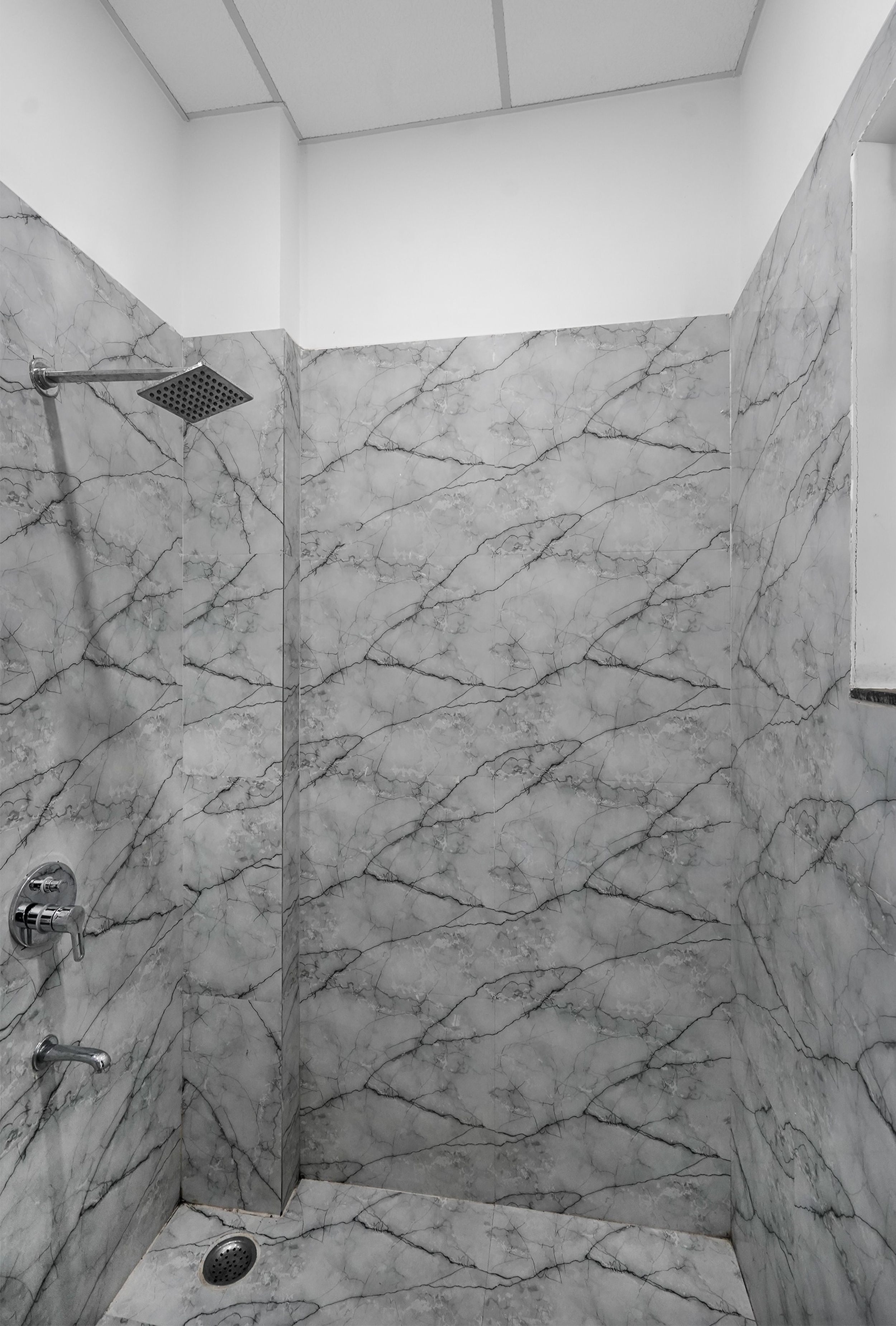 Eine Dusche mit Glastür und Regendusche, eingebettet in einen Raum mit Marmor-Musterwänden.