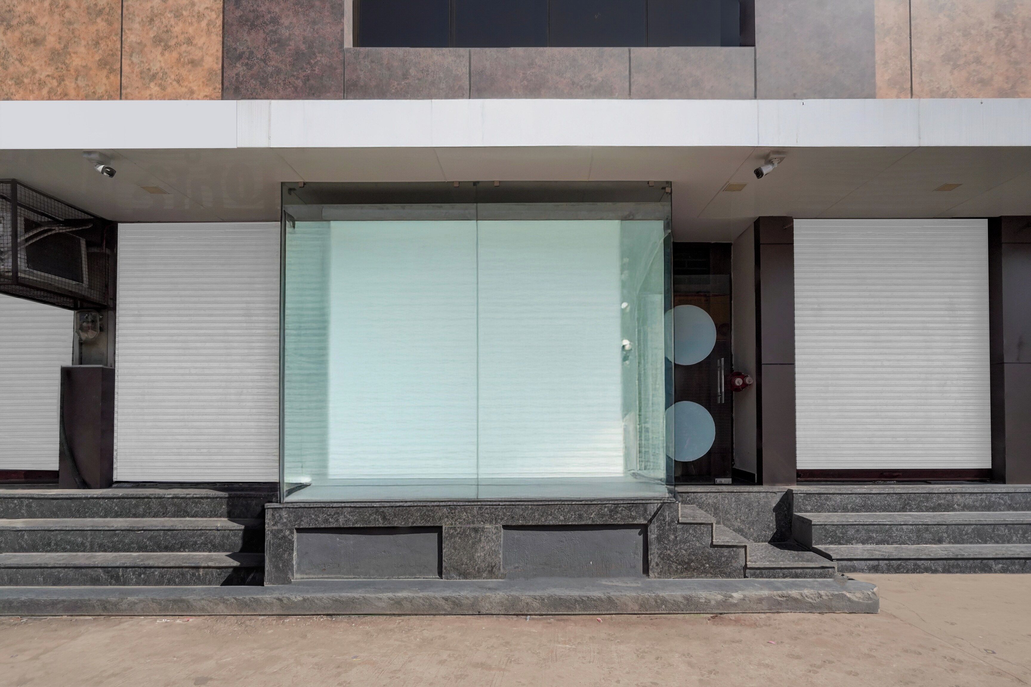 Un edificio moderno con un gran ventanal, una escalera que lleva a la entrada y contraventanas cerradas a ambos lados.