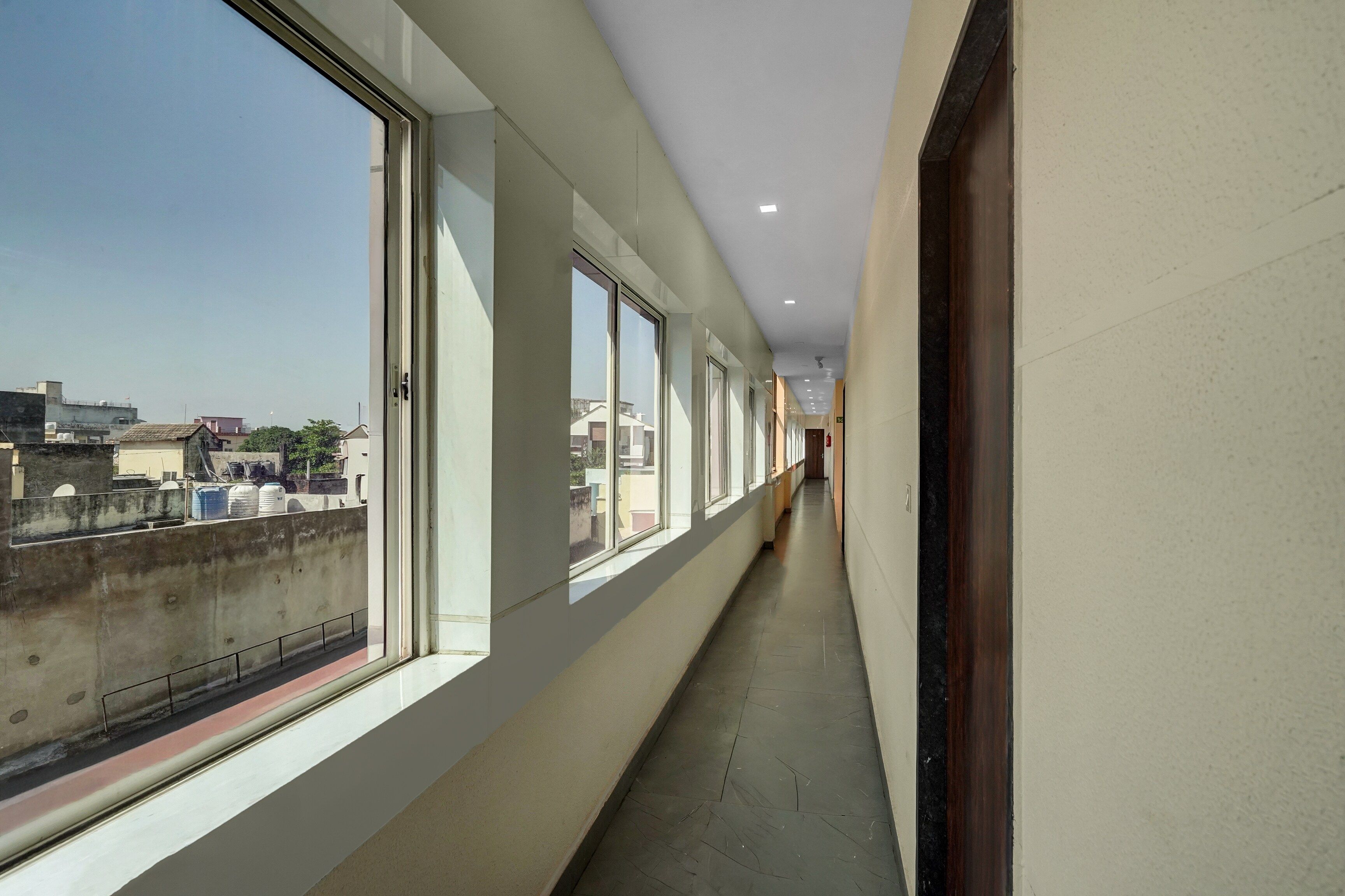 Un pasillo con grandes ventanales, piso de baldosas y vista a edificios.