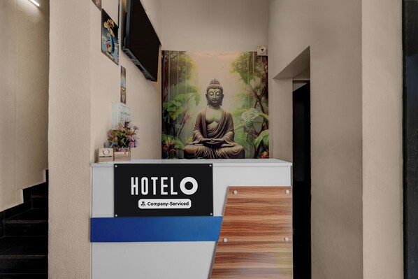 A reception desk with a sign reading 'HOTEL Company Serviced' and a Buddha statue in the background.