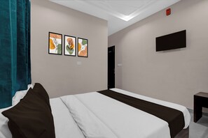Ein Hotelzimmer mit einem Bett, einem an der Wand befestigten Flachbildfernseher und drei gerahmten Kunstwerken an der Wand.