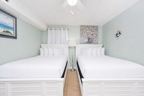 Una habitación de hotel con dos camas, un ventilador de techo, un cuadro en la pared y una mesita con una lámpara.
