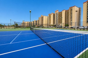 A tennis court with a net, surrounded by high-rise buildings. - Phoenix Ii 2098 3 Bedroom Condo (Orange Beach)